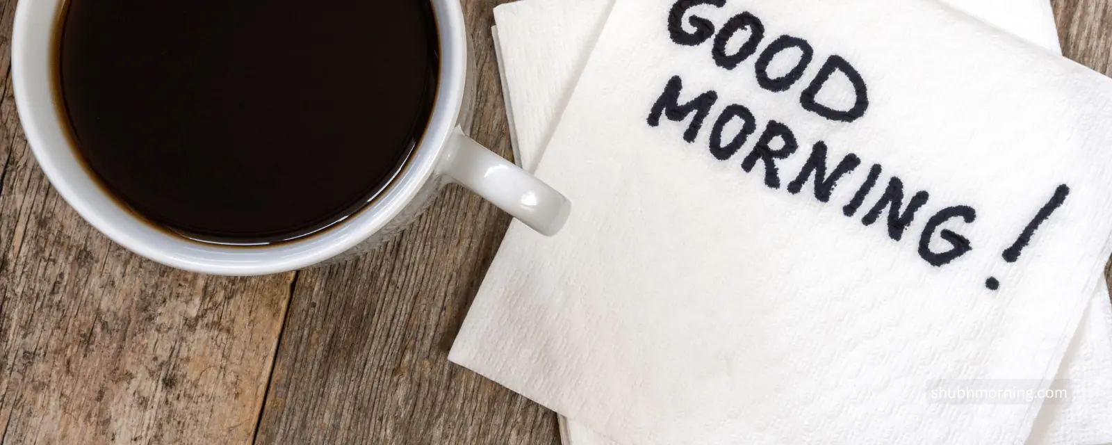 Good Morning written on a napkin beside a mug of black coffee on weathered wood