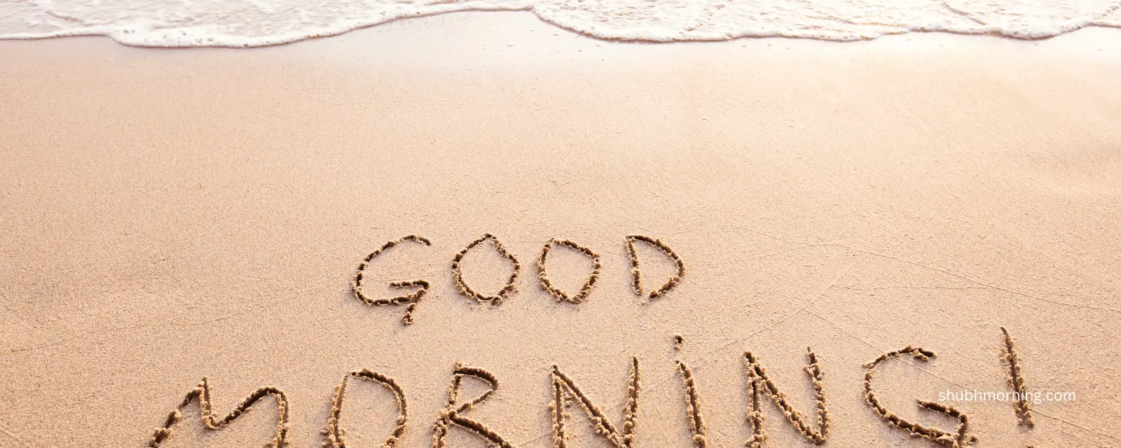 Good Morning written in wet beach sand as a wave washes in